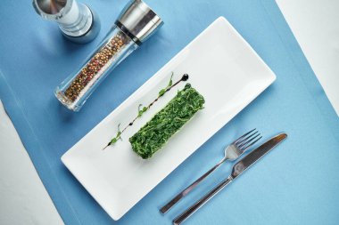 Ana yemekler için nefis bir meze. Mavi masa örtüsü üzerinde beyaz tabakta kremalı ıspanak.