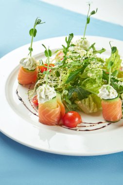 Deniz ürünleri, somon, roka ve kiraz domatesli iştah açıcı salata mavi masa örtüsü üzerinde beyaz bir tabakta.