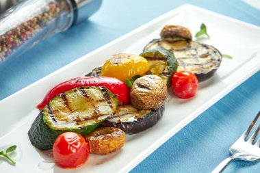 Hafif ve diyet sebzeler, biberler, kabak, mavi masa örtüsü üzerinde beyaz bir tabakta mantarlar..