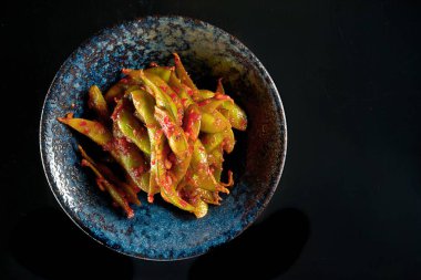 Baharatlı kırmızı soslu fasulye salatası, koyu bir kasede servis edilir. Siyah bir arka planda izole edilmiş. Restoran yemeği. Japon mutfağı