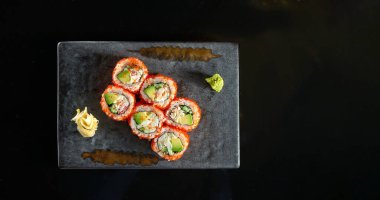 Yengeç, avokado, salatalık ve tobiko havyarlı California suşi rulosu wasabi ve zencefil ile servis edilir. Siyah arka planda izolasyon. Japon yemeği.
