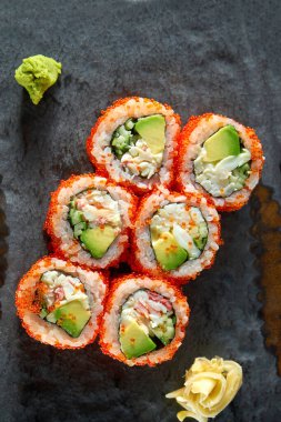 Yengeç, avokado, salatalık ve tobiko havyarlı California suşi rulosu wasabi ve zencefil ile servis edilir. Siyah arka planda izolasyon. Japon yemeği.