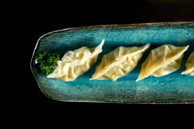Ağız sulandıran Asya gyozası, deniz ürünleriyle doldurulmuş, mavi bir tabakta servis ediliyor. Japon Jiaozi ya da siyah arka planda izole edilmiş börekler. Pan-Asya mutfağı