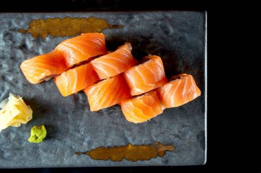 Somon, yılan balığı, avokado ve tobiko havyarla iştah açıcı kırmızı ejderha suşi rulosu, seramik tabakta zencefil ve wasabi ile servis ediliyor. Siyah bir arka planda izole edilmiş. Japon yemeği.