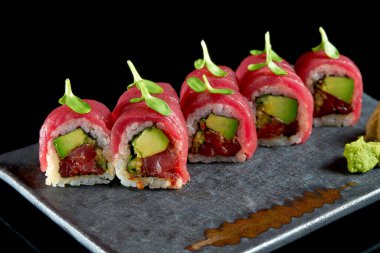 Ton balığı, avokado ve salatalık ile nefis suşi rulosu, seramik tabakta zencefil ve wasabi ile servis edilir. Siyah bir arka planda izole edilmiş. Japon yemeği.