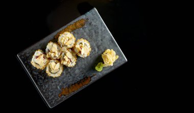 Ton balığı, fıstık, patlamış mısır ve salatalık ile nefis çıtır suşi rulosu, seramik tabakta zencefil ve wasabi ile servis ediliyor. Siyah bir arka planda izole edilmiş. Japon yemeği.