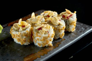 Ton balığı, fıstık, patlamış mısır ve salatalık ile nefis çıtır suşi rulosu, seramik tabakta zencefil ve wasabi ile servis ediliyor. Siyah bir arka planda izole edilmiş. Japon yemeği.