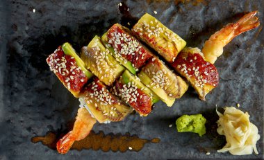 Wasabi ve zencefilli bir tabakta servis edilen tempura karides, avokado ve yılan balığı ile lezzetli suşi rulosu. Siyah arka planda izolasyon. Japon yemeği. Altın ejder