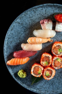 Kaliforniya suşi sarması, tobiko havyarlı somon balığı ve çeşitli suşiler. Somonlu suşi, ton balığı, karides. Japon dürümleri mavi bir tabakta servis edilir. Siyah arkaplanda izole