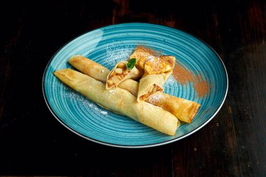 Geleneksel Ukrayna krepleri, koyu arkaplanda domatesli ve ekşi kremalı mavi bir tabakta servis edilir. Doldurulmuş Ukrayna Blini