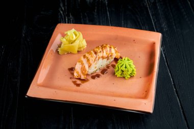 Füme somon ve unagi soslu Japon nigiri, siyah ahşap arka planda zencefil ve wasabi ile servis edilir.