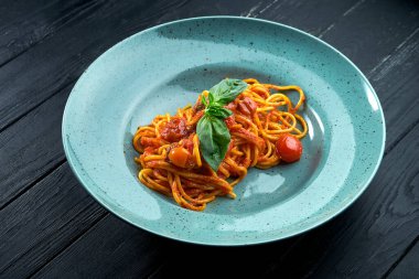 Geleneksel makarna spagetti Arrabbiata sosu (kırmızı sarımsak, paprika ve domates ile) fesleğenli, siyah, ahşap arka planda mavi bir tabakta servis edilir.