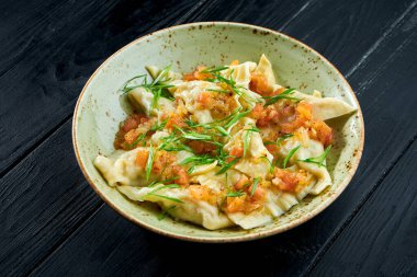 Geleneksel İsrail mutfağı yemeği. Domates salsa soslu tavuk kreplach ve siyah ahşap arka planda yeşil soğan. Restoran yemeği. Farklı dolgulu börekler.