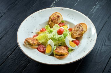 Parmesanlı Sezar salatası, pastırma, tavuk, ahşap arka planda siyah tabakta yumurta. Restoran servisi. Kopyalama alanı ile kapat.