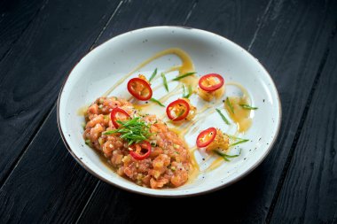 Lezzetli aperatif: Avokado ile somon tartar ve siyah ahşap arka planda beyaz tabakta acı biber..