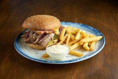 Domuz eti, soğan, domates, patates kızartması ve sosla süslenmiş domuz pastırmalı iştah açıcı Amerikan hamburgeri. Ahşap arkaplan