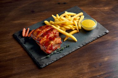 İştah açıcı bira aperatifi, bal soslu barbekü domuz pirzolası ve siyah tabakta servis edilen patates kızartması. Ahşap arkaplan.