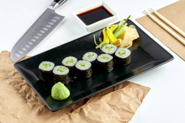 Klasik Japon suşi rulosu - salatalık hosomaki, siyah tabakta servis edilir. Beyaz arka plan. Yuvarlak maki