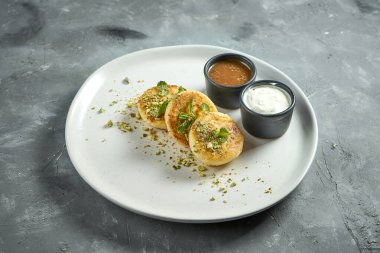 Ev yapımı peynirli kekler ya da beyaz tabakta reçelli ve ekşi kremalı Syrniki. Ukrayna yemeği. Kahvaltılık yemek. Süzme peynirli börek