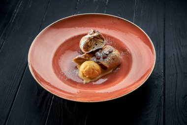 İştah açıcı Avusturya hamur tatlısı. Tatlı soslu ve sarı dondurmalı elmalı turta. Koyu bir arka planda servis ediliyor..