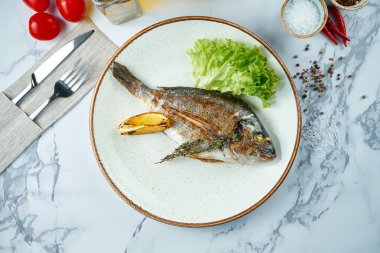 İştah açıcı ve diyet ızgara Dorado, mermer arka planda beyaz bir tabakta servis ediliyor. Üst görünüm