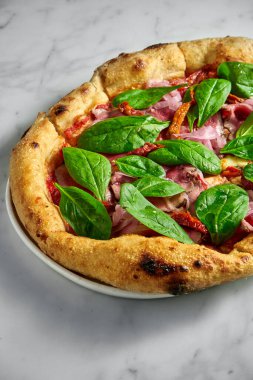 Biftekli lezzetli pizza, güneşte kurutulmuş domates, soğan turşusu, beyaz mermer arka planda beyaz bir tabakta peynir ve ıspanak.