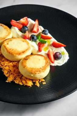 İdeal bir kahvaltı - Beyaz soslu süzme peynirli krep, çilek, çilek ve mermer arka planda siyah bir tabakta çıtır çıtır. Ukrayna şurubu