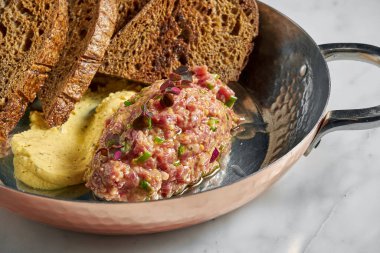 Lezzetli aperatif, biftekli tartar, sarı sos ve çavdar ekmeği, mermer arka planda bakır bir tabakta servis edilir..