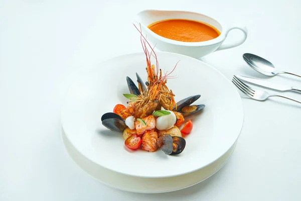 Delicious red Bouillabaisse soup in a special bowl. salmon, scallop, langoustines and mussels served in a white plate on a white tablecloth. tomato soup with seafood