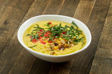 İştah açıcı ve diyet yemeği - kremalı mısır çorbası ve kızarmış mantar, domates ve otlar ahşap arka planda beyaz bir kasede.