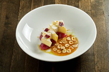 Lezzetli aperatif - fındıklı fırında peynir, üzüm ve karamel bal sosu, ahşap arka planda beyaz bir tabakta servis ediliyor. Peynir fondüsü