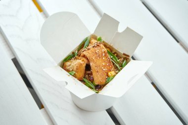 Sebzeli, soğanlı, soslu ve soya peynirli Asya usulü erişteler beyaz bir tahta tabakta servis ediliyor. Yemek servisi için fotoğraf.