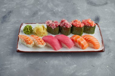 Somon, ton balığı, krevekta ve yılan balığı ile iştah açıcı suşi ve gunkanlar, gri arka planda beyaz bir tabakta baharatlı sos. Japon yemeği.