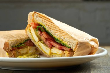 Tofu, domates ve pesto soslu büyük boy kızarmış sandviç. Ahşap arka planda beyaz bir tabakta servis ediliyor.