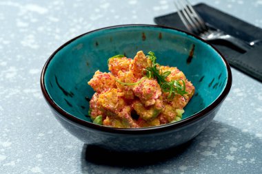 İştah açıcı aperatif, soslu kızarmış karides patlamış mısır, tobiko havyar ve gri arka planda mavi bir kasede avokado. Yaklaş, seçici odaklanma