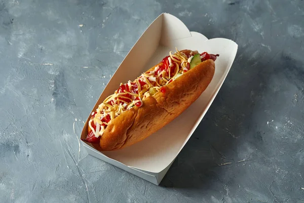 Appetizing hot dog with hot peppers, onions, smoked sausage in a white box on a gray background