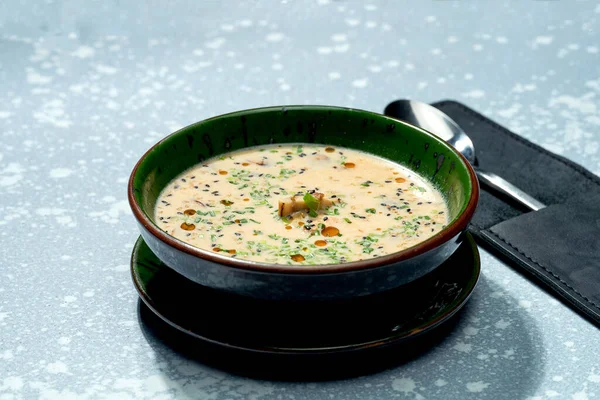 Appetizing dish of pan-asian cuisine - cheese miso soup in a green bowl on a gray background