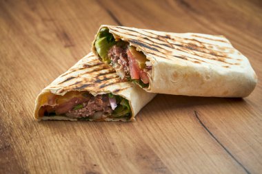 Ahşap arka planda servis edilen, sebzeli, soslu ve etli aperatif çörek. Geleneksel sokak yemekleri - shawarma