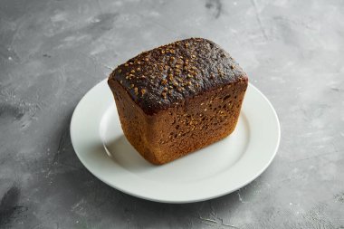 Gri arka planda beyaz tabakta koyu çavdar ekmeği.