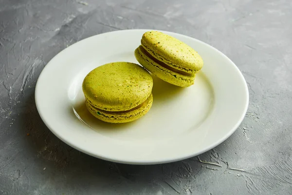 Aperatif badem unu Macaroon kurabiyeleri ve şam fıstıklı dahili katman gri arka planda beyaz bir tabakta servis ediliyor.