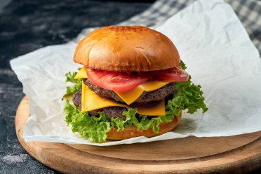 Biftekli, domatesli, marullu, beyaz parşömende erimiş peynirli leziz çift katlı burger. Karanlık arka plan. Amerikan fast food