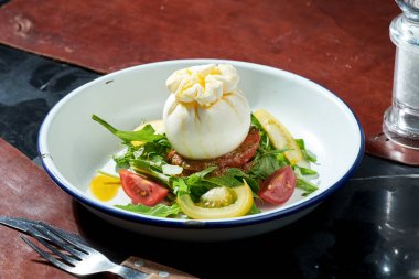 Mozzarella burrata, roka, pesto, beyaz tabakta kiraz domatesli salata. Karanlık arka plan. Sert ışık