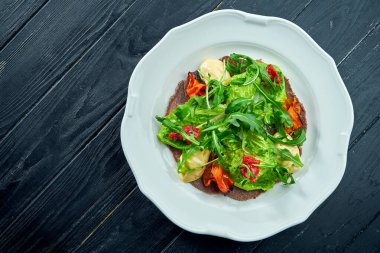 Geleneksel İtalyan aperatif salatası vitello tonto 'dur. İnce dilimlenmiş biftek, roka, domates ve pesto, beyaz bir tabakta servis edilir.