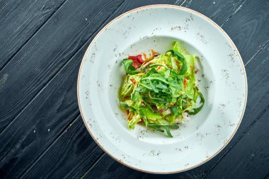 İştah açıcı, roka soslu diyet salatası, marul ve siyah ahşap arka planda beyaz tabakta sıcak et. Sağlıklı yemek.