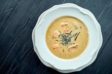 Somon, nori ve susam tohumlu Hindistan cevizi çorbası, koyu ahşap arka planda beyaz bir tabakta servis ediliyor. Pan-Asya mutfağı