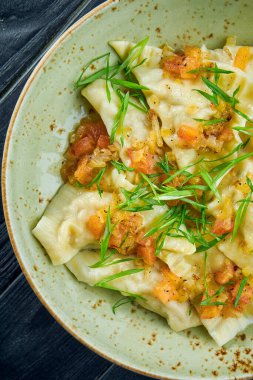 Geleneksel İsrail mutfağı yemeği. Domates salsa soslu tavuk kreplach ve siyah ahşap arka planda yeşil soğan. Restoran yemeği. Farklı dolgulu börekler.