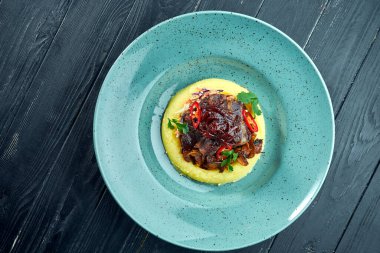 İştah açıcı yemek. Izgara sığır eti yanağı. Siyah ahşap arka planda mavi bir tabakta patates püresi ile süslenmiş. Kapat.