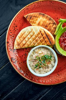 Geleneksel İsrail ya da doğulu Baba ghanoush sebze salsa ve pita ile koyu arka planda kırmızı bir tabakta servis edilir. Patlıcan lokantası yemeği