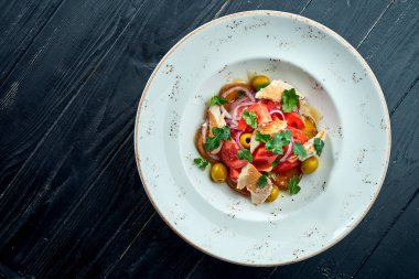 İştah açıcı, domatesli diyet salatası, soğan, zeytin ve siyah ahşap arka planda beyaz tabakta ızgara alabalık. Sağlıklı yemek.