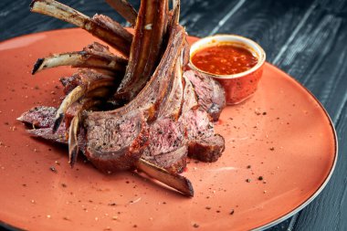 Izgara kuzu ızgarasında iştah açıcı, koyu arkaplanda kırmızı sosla servis edilmiş. B-B-Q